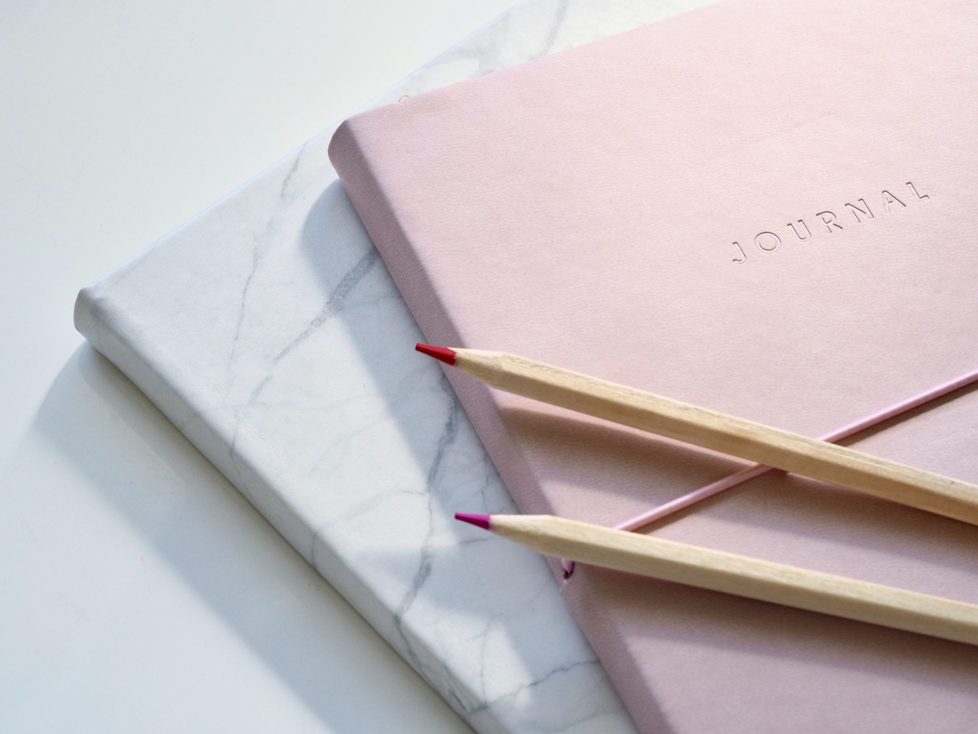 Two pencils are laying on a pink notebook.