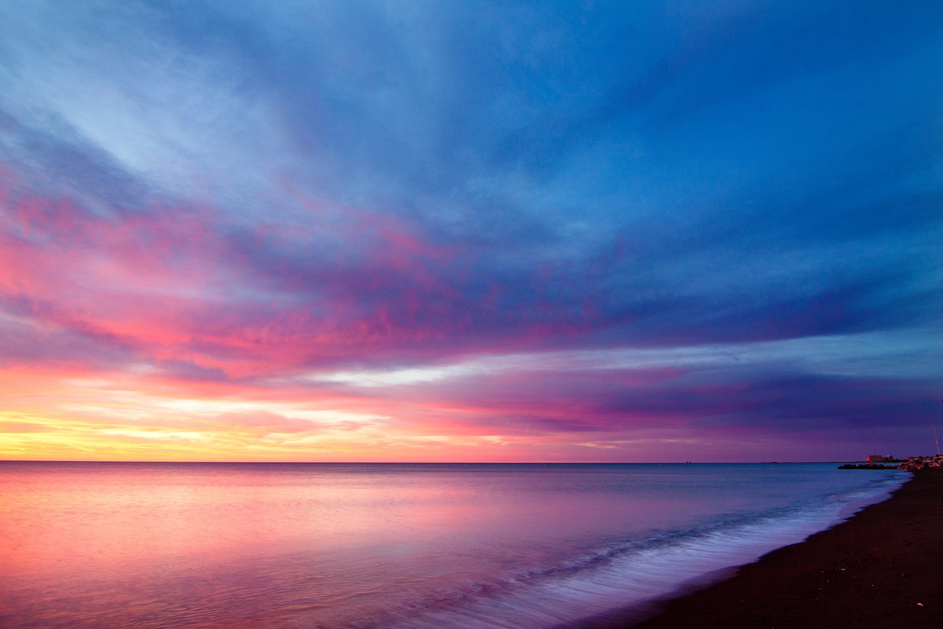 A sunset over the ocean with pink and blue clouds.