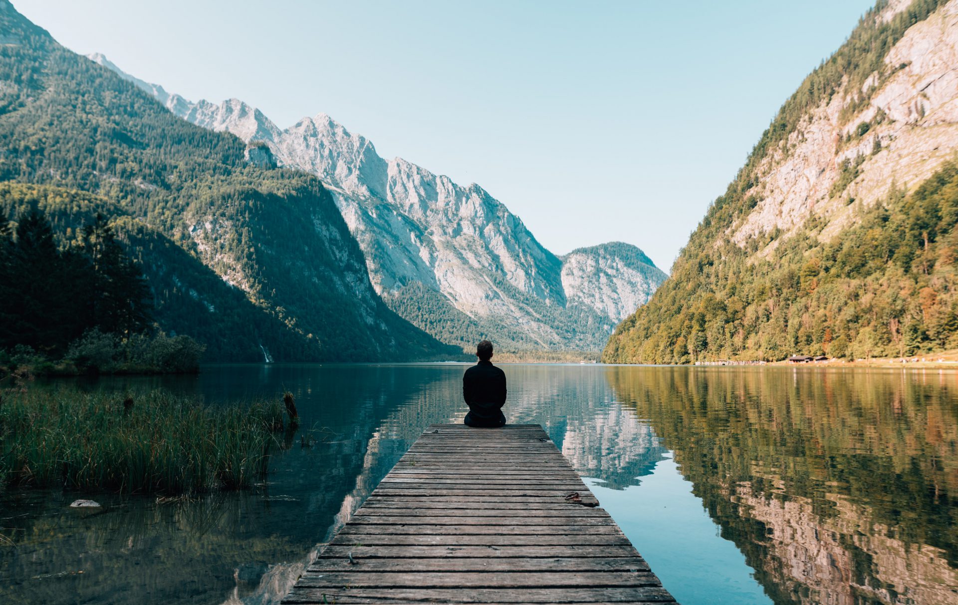 A person sitting on the end of a dock in front of some mountains