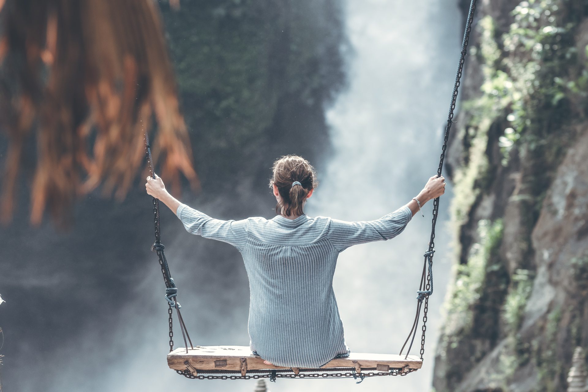 A person on a swing in front of a waterfall.