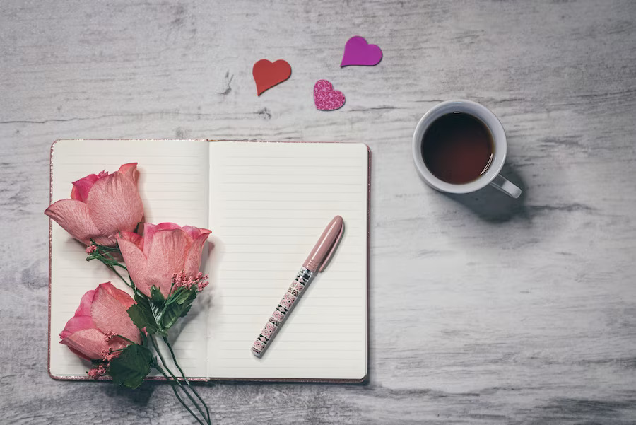 A cup of coffee, pen and roses on the table.