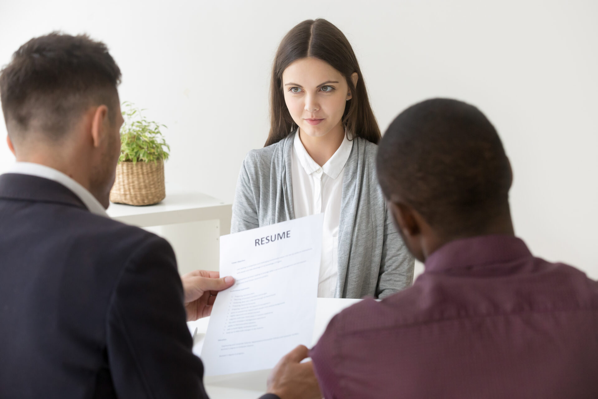 A woman is holding up her resume while two men look on.