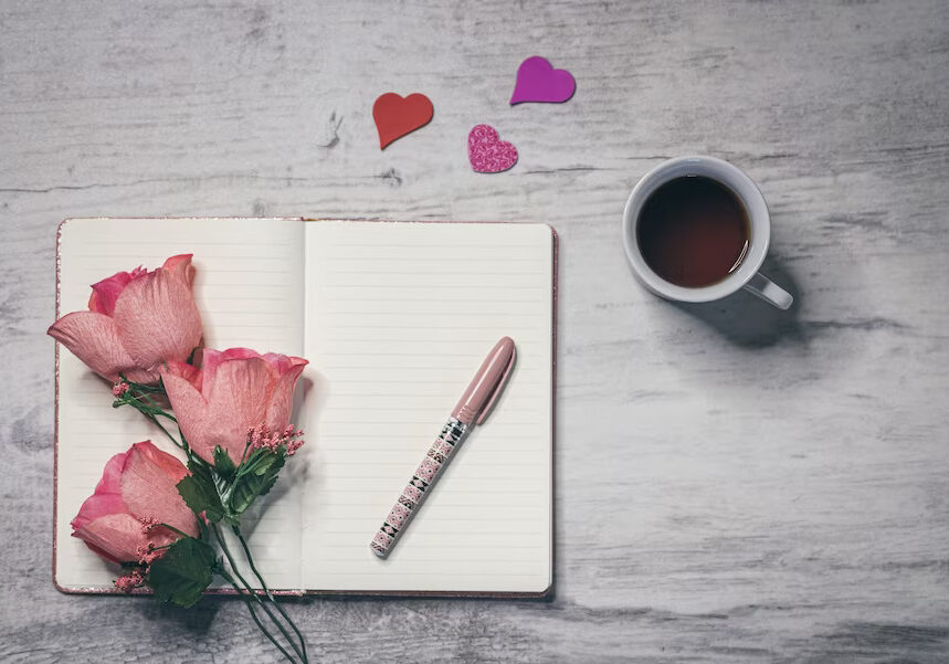 A cup of coffee, pen and roses on the table.