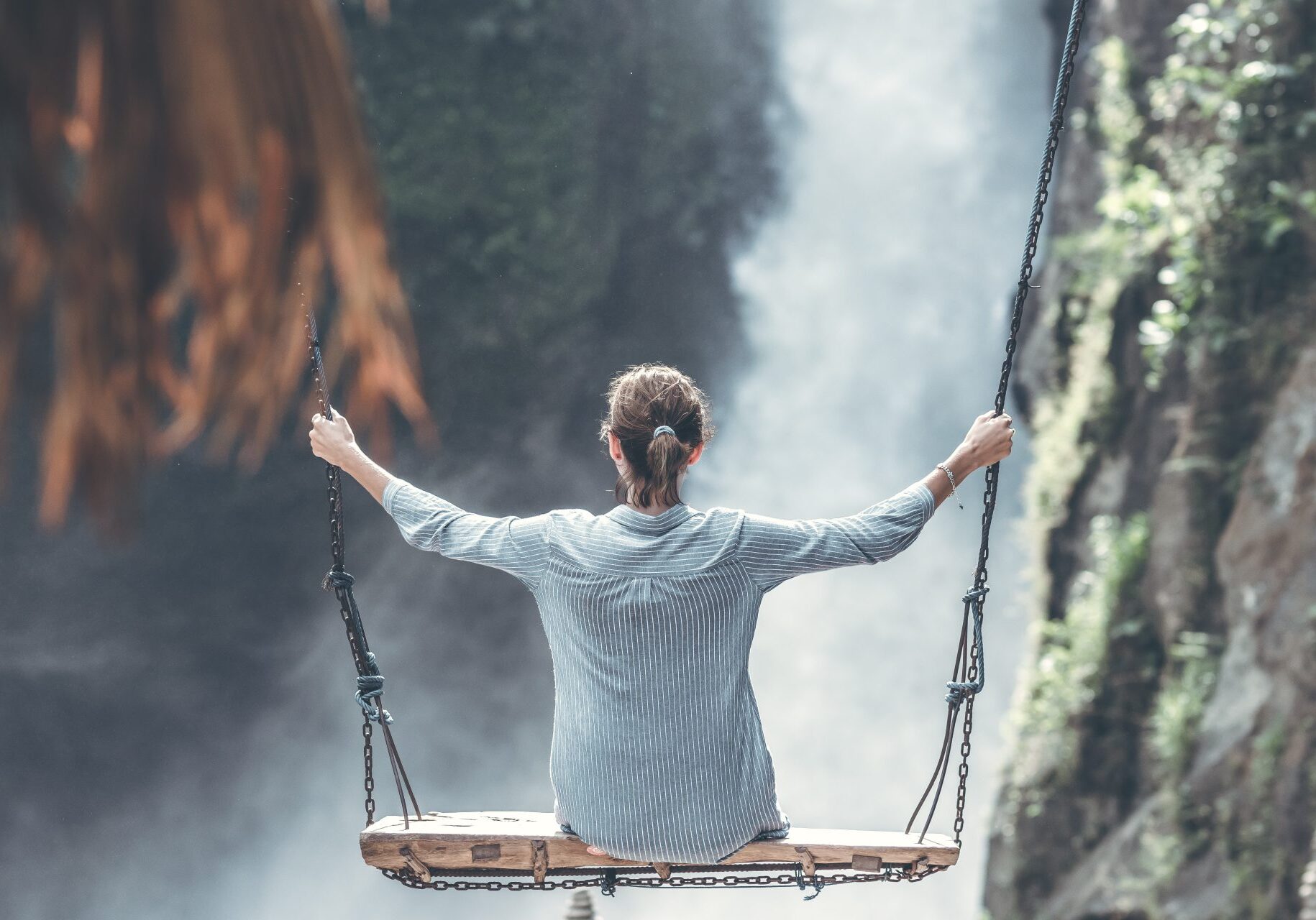 A person on a swing in front of a waterfall.