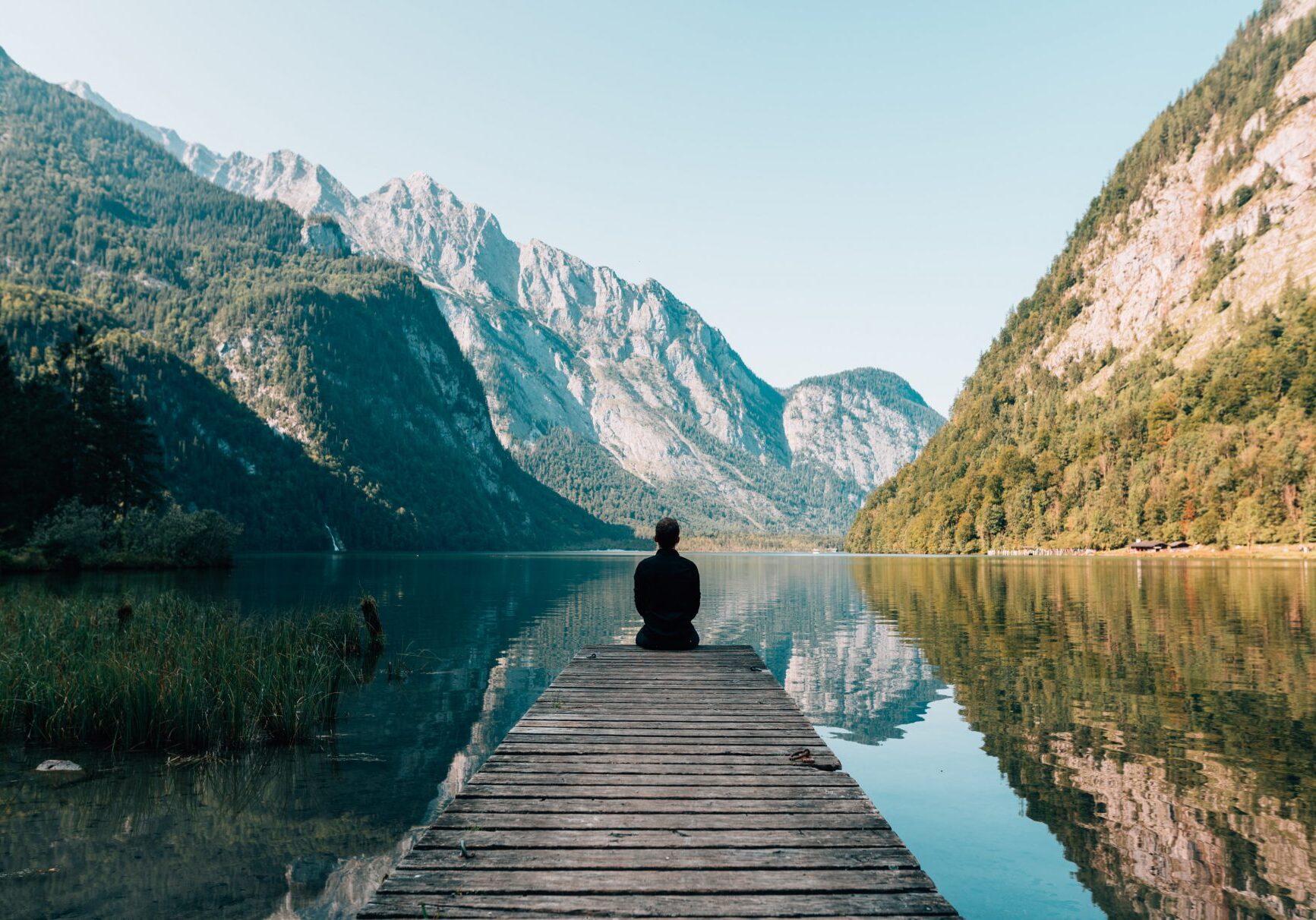 A person sitting on the end of a dock in front of some mountains