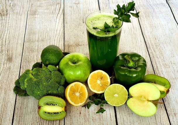 A green smoothie surrounded by fruits and vegetables.